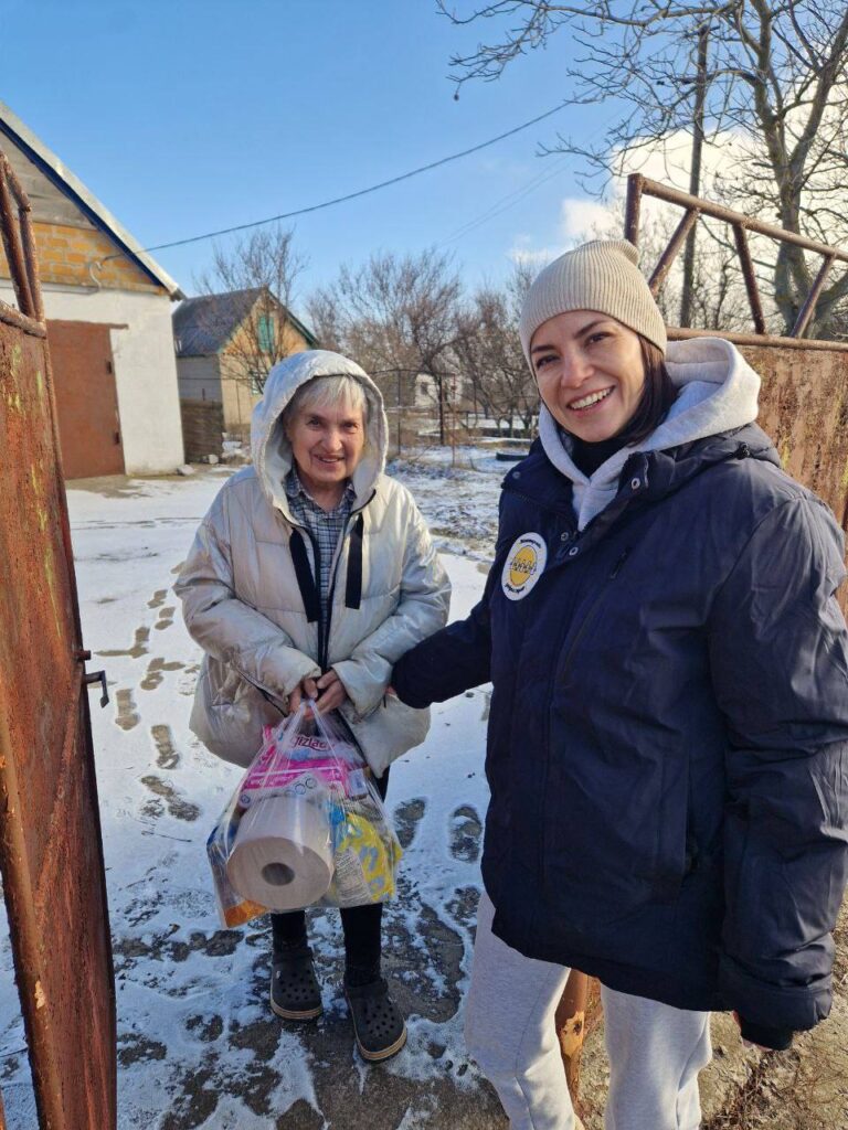 Волонтер передає пакет із допомогою літній жінці.